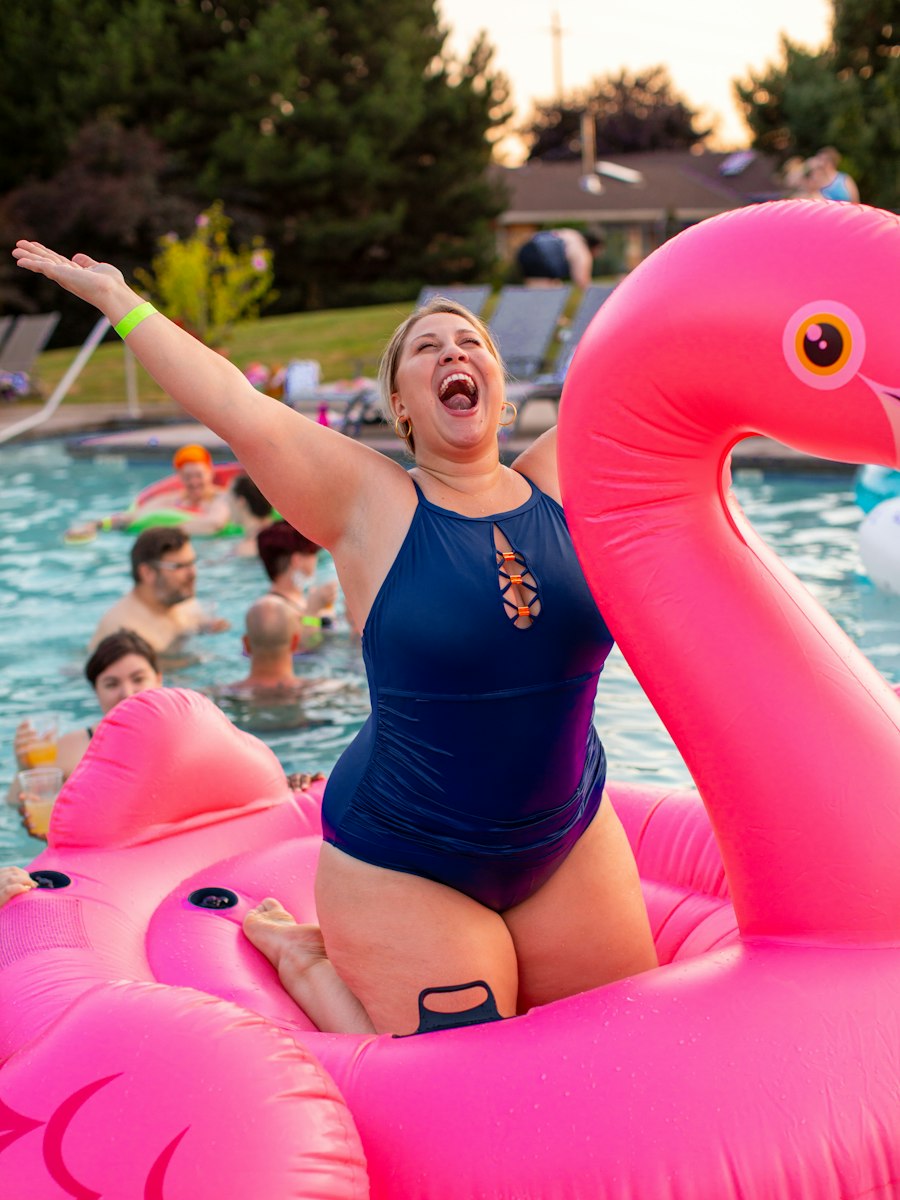 Woman in a navy swimsuit laughing on a pink flamingo float